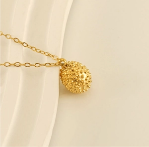 Macro shot of 18k gold plated durian pendant necklace with textured metallic surface