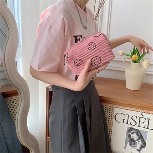 Pink corduroy makeup bag with black smiley patterns held by hand in a cozy home setting