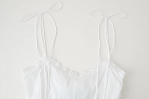 Detail of white spaghetti strap top with knotted shoulders and ruffled neckline
