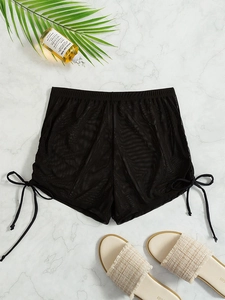 Detail of sheer black mesh beach shorts with side drawstring ties and ruched texture