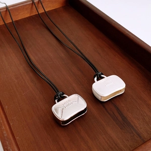 Macro detail of miniature handbag pendants with engraved logo on black cord necklaces