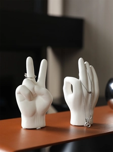 Detail view of white ceramic hand-shaped jewelry stands holding rings and necklaces