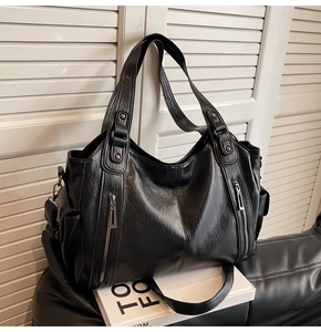 Detail view of large black tote bag with dual handles and side zipper on leather seat