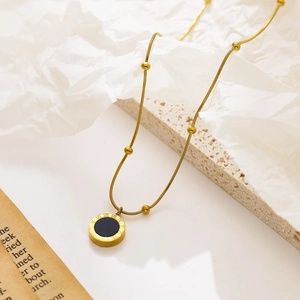 Detail of gold titanium necklace with Roman numerals and black enamel pendant on stone