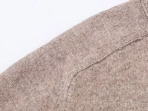 Close-up of beige knit cardigan fabric showing detailed texture and seam stitching