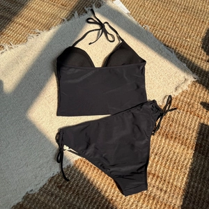 Flat lay of black halter neck bikini set with side-tie bottoms on a resort style background