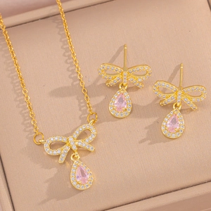 Golden jewelry set with zircon bow and pink teardrop pendant in a beige gift box