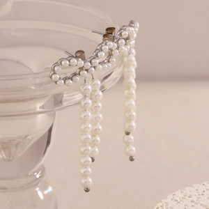 Detailed view of silver bow-shaped pearl drop earrings hanging on a glass rim