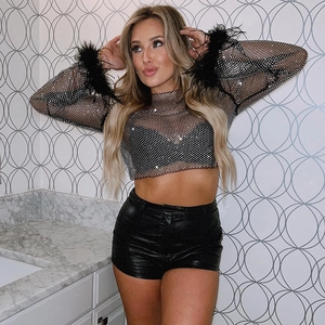 Détail du haut en maille strass noire avec poignets en plumes et short en cuir taille haute