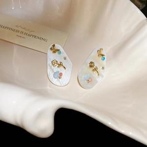 Détail de boucles d'oreilles ovales à texture coquillage, roses dorées et cristaux