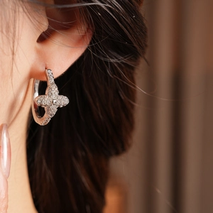 Close-up of sparkling zircon clover earring worn on ear with elegant silver finish
