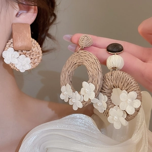 Close-up of bohemian rattan hoop earrings with white fabric flowers and pearls details