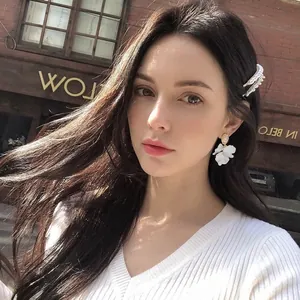 Elegant white shell flower earrings and textured hair clip worn by a model in outdoor setting