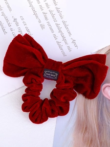 Detail of red velvet bow hair clip featuring a gold Hand Made label on textured fabric