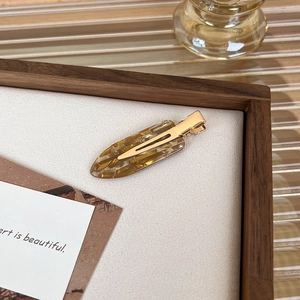Detail of amber tortoiseshell cellulose acetate hair clip with gold metal base on white background