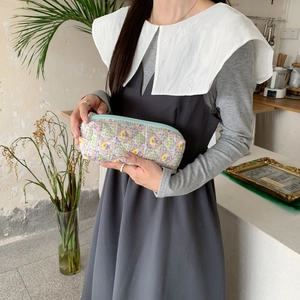 Dettaglio di trousse floreale trapuntata con zip blu tenuta a mano in un ambiente luminoso