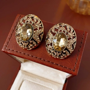 Macro detail of vintage gold oval hollow earrings with champagne rhinestones on red leather