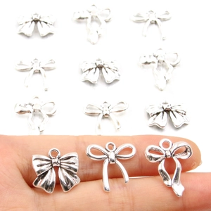 Assorted silver alloy bow pendants held in hand for DIY necklace and bracelet crafting