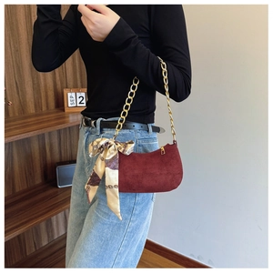 Detail of burgundy suede shoulder bag with gold chain strap and decorative silk scarf