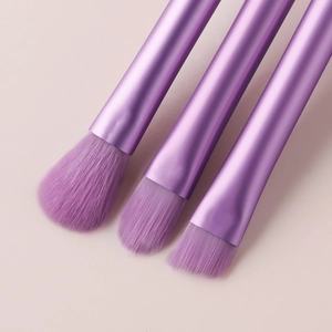 Close-up of three mini makeup brushes with crystal purple handles on a soft pink background