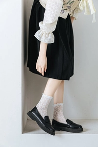 Detailed view of white mesh lace calf socks styled with black loafers and a pleated skirt