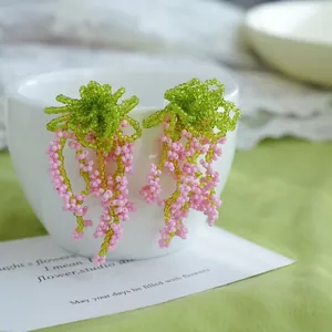 Détail de boucles d'oreilles faites main en perles glycine avec pompons roses sur tasse