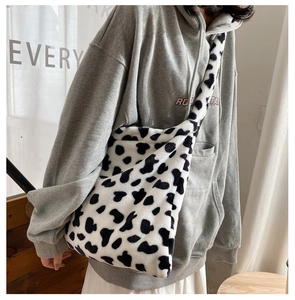 Close-up of a large fluffy cow print plush crossbody bag styled with casual grey hoodie