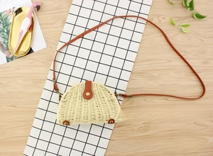 Detailed close-up of semi-circular straw bag with brown PU leather flap and metal buckle