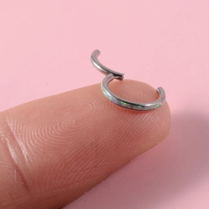 Makroansicht eines G23 Titan Piercing-Rings mit buntem Opal-Inlay auf einer Fingerspitze