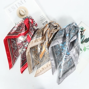 Three silk-like paisley square scarves in red, gold, and blue on a styled white background