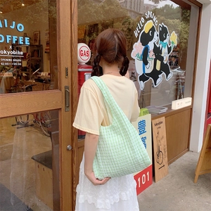 Green and white checkered canvas tote bag shown on model back in a cozy cafe setting