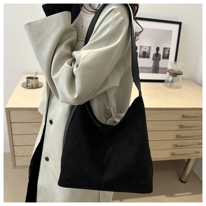 Detail view of the black matte suede tote bag worn by a model in a warm home setting