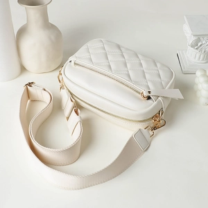 White quilted crossbody bag with wide strap and gold zipper on minimalist background