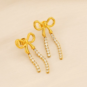 Detailed close-up of gold bow earrings with shimmering rhinestone tassels on beige fabric