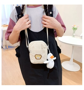 Close-up of beige corduroy shoulder bag featuring bear embroidery and white duck plush charm