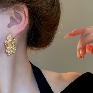 Close-up of gold star-shaped earrings with textured surface and sparkling rhinestones