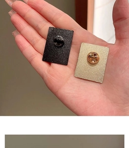Detail view of rectangular metal brooch backs in matte black and gold textured finish