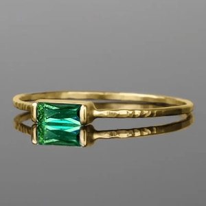 Detailed close-up of a gold-tone hammered ring band featuring a green rectangular emerald stone