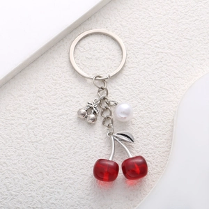 Detail of red cherry pendant with pearl and silver chain on a textured surface
