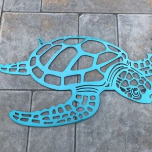 Turquoise metal sea turtle wall art with hollow design placed on a stone surface