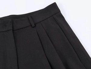 Detailed view of black wide-leg trousers featuring belt loops and pleated fabric design