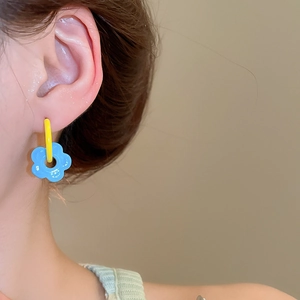 Macro side view of a model wearing colorful flower hoop earrings with blue floral pendant
