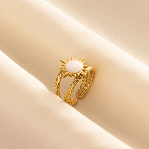 Golden sunburst ring with white oval gemstone on a beige silk fabric background