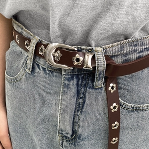 Close-up of vintage brown leather belt with silver floral eyelets on denim jeans
