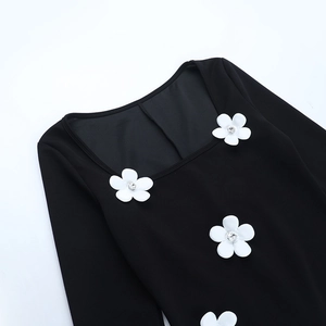 Détail du décolleté carré avec fleurs 3D blanches sur une robe noire à manches longues