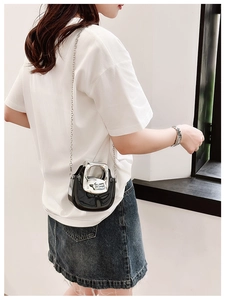 Mini black patent leather crossbody bag with silver metal handle worn by a model