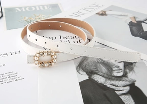 Detailed view of a white leather dress belt featuring a pearl and rhinestone oval buckle