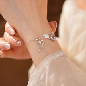 Detail of silver bracelet featuring bow, star, and pink heart charms on model wrist