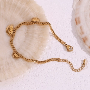 Detail of 18K gold plated stainless steel bracelet with sun pendants on coral background