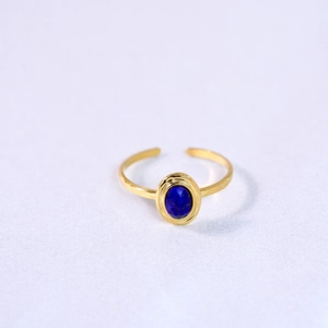 Detail of a gold adjustable ring with an oval dark blue natural stone on a white surface
